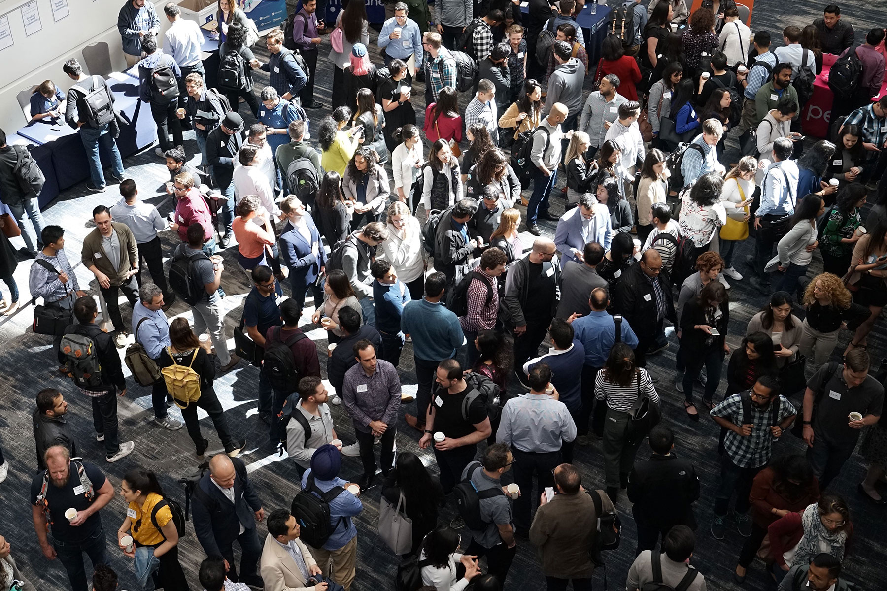 Large crowd of people standing and browsing booths in a convention setting